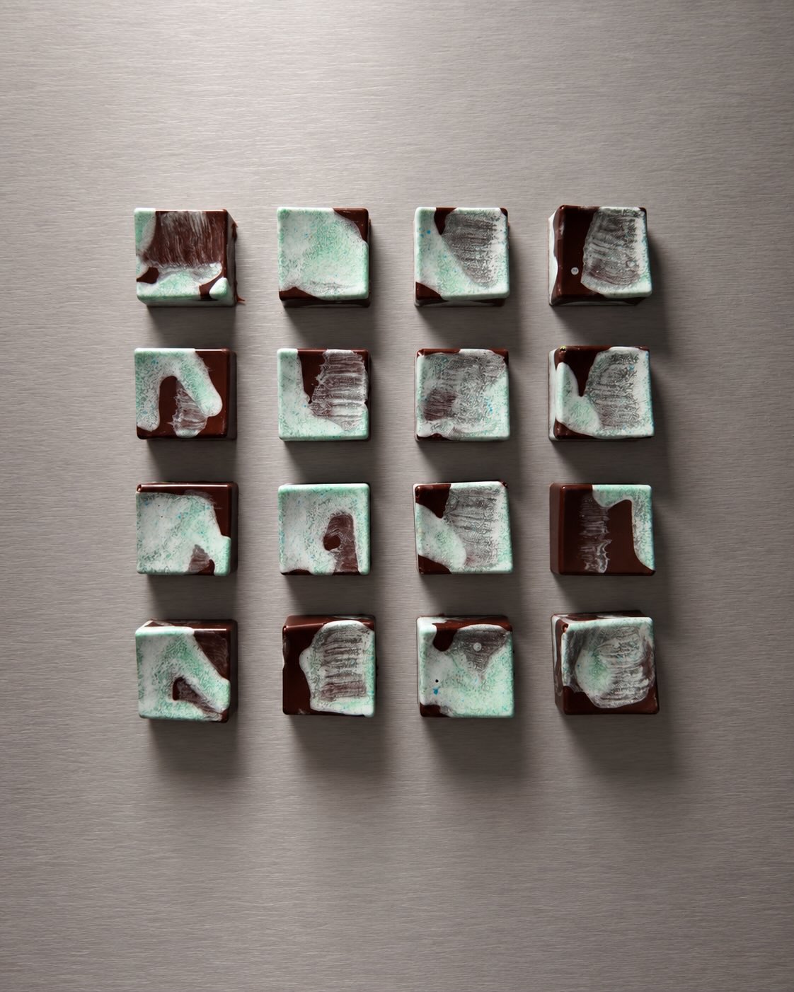 Sixteen hand-painted chocolate bonbons in a grid